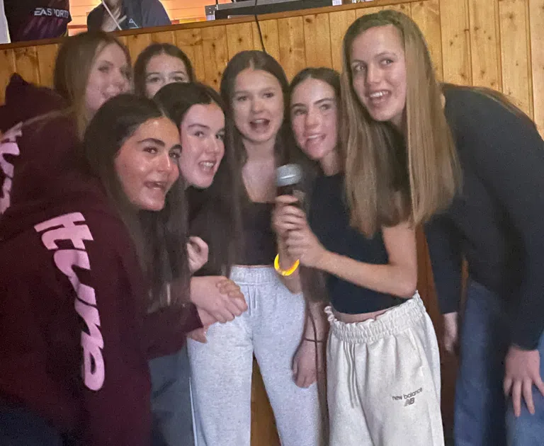 Group of friends posing indoors, one girl holding a microphone as they smile for the camera in a wood-paneled room.