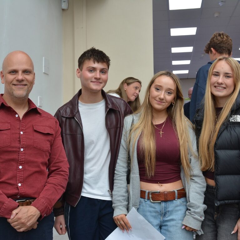 Group of five people standing in a school hallway, smiling at the camera.