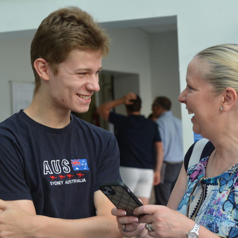 Teenager and an older woman smiling at each other as the woman shows something on her smartphone.